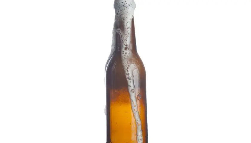 Bière débordant d'une bouteille, la mousse blanche montant. Le pourcentage d'eau dans la bière est élevé, comme le montre cette effervescence.