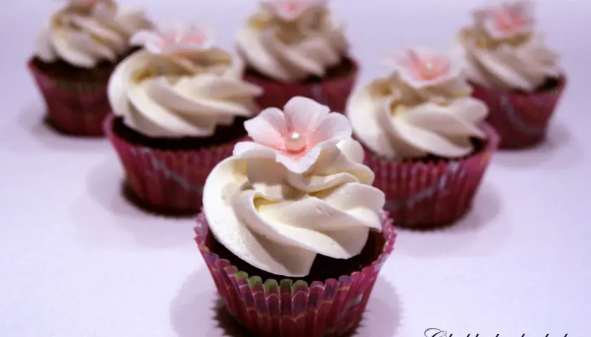 Sju små mini cupcakes med vit frosting och rosa blommor. Perfekta för ett sött kalas.