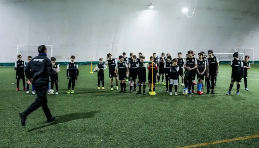 Trener prowadzi trening piłkarski metodą Coerver Coaching, instruując młodych zawodników na boisku.
