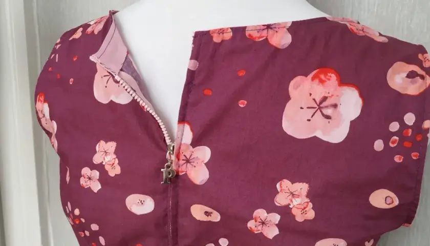 A plum-colored dress with a floral print features a centered zipper with a silver "P" charm.
