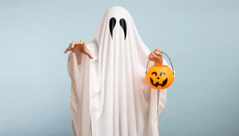 Bambino con costume da fantasma fai da te, tiene un cestino di caramelle a forma di zucca.