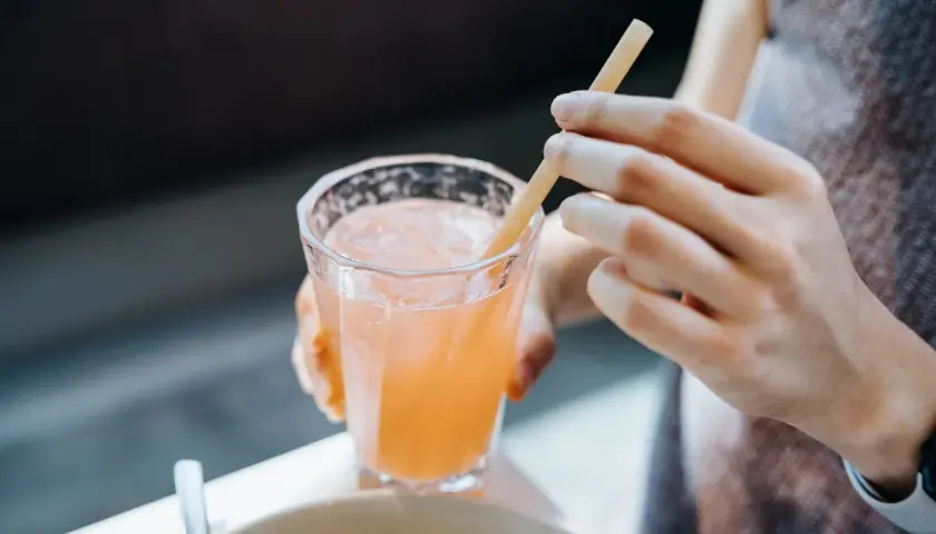 Glas mit rosafarbenem Getränk und Eis, eine Hand hält einen Strohhalm. Vielleicht ein gesunder Drink mit Sauerkrautsaft Inhaltsstoffe.