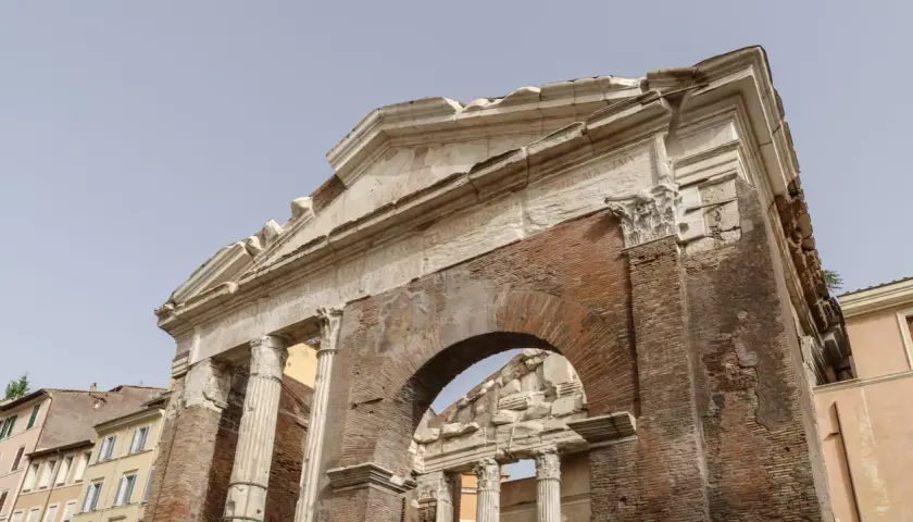 Antica struttura in mattoni e marmo, con colonne e un arco, parte del **Portico di Ottavia**.