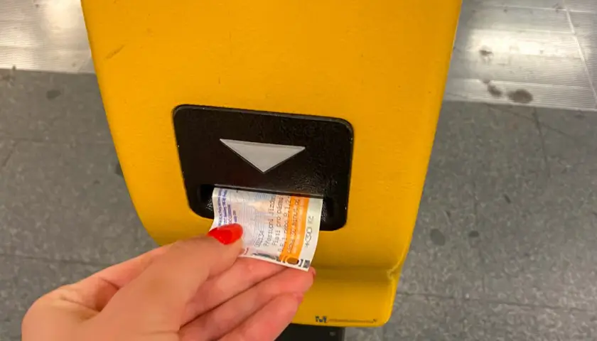 Dłoń z czerwoną hybrydą wkłada bilet do żółtego automatu w praskim metrze. Bilety na metro w Pradze są łatwe do kupienia.