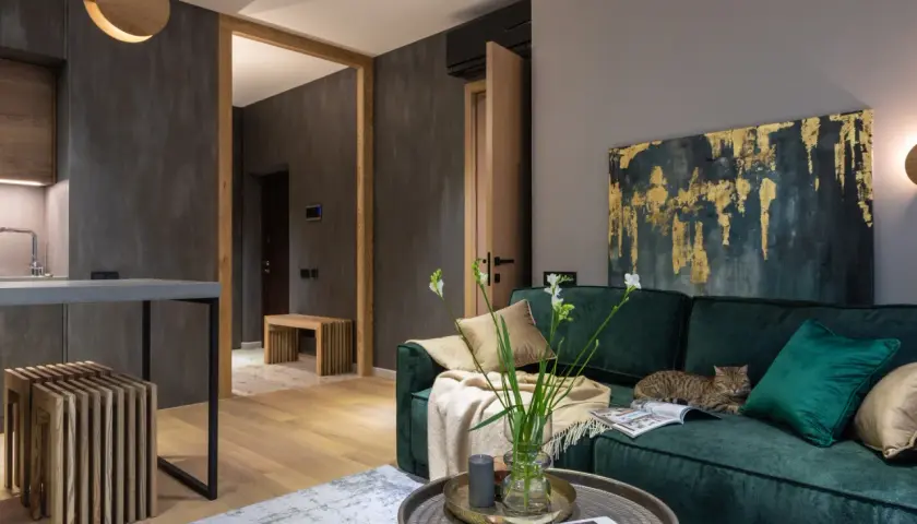 Elegancki salon z butelkowozieloną kanapą, na której leży kot. Złoto-granatowy obraz i jasne dodatki pokazują, jaki kolor pasuje do zielonego butelkowego.