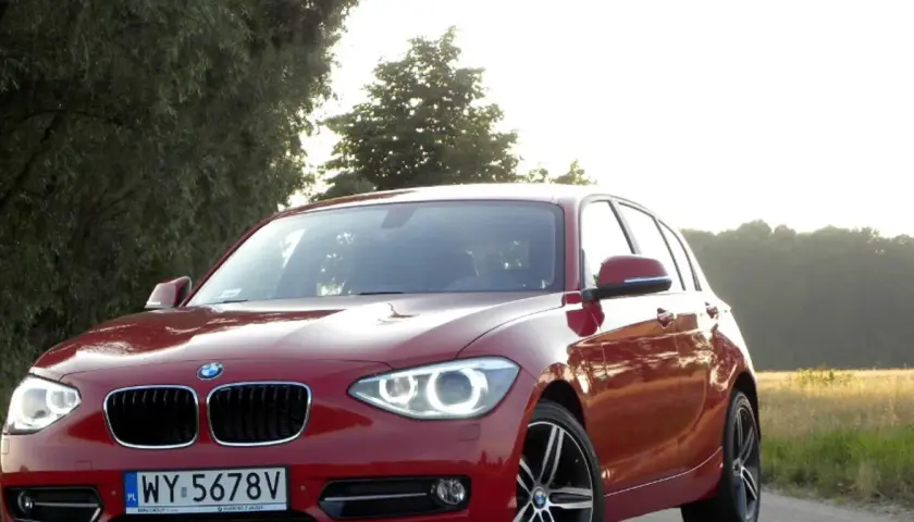 Czerwone BMW 118d na tle drzew i pól.