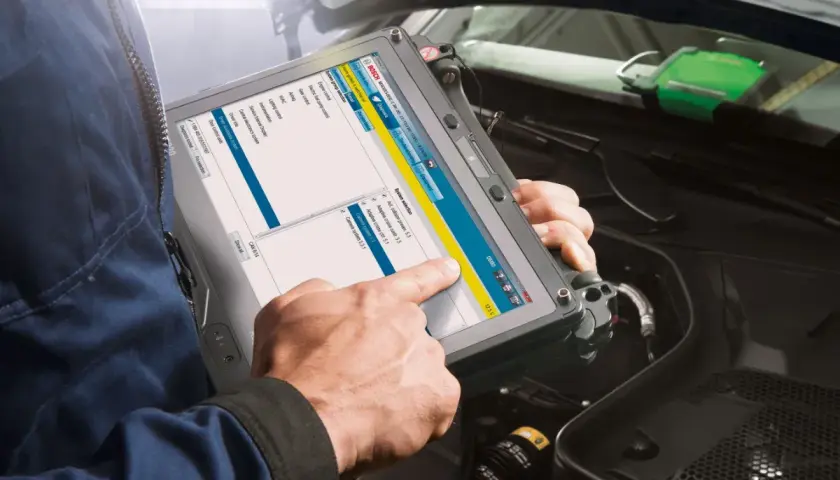 Mechanik sprawdza wtryski za pomocą tabletu diagnostycznego Bosch. Na ekranie widoczne są opcje wyboru systemu, w tym silnik i systemy sterowania.
