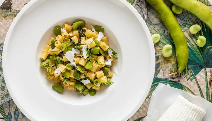 Piatto di pasta con fave fresche, un assaggio della ricetta pasta con le fave fresche alla siciliana, guarnita con ricotta salata e erbe aromatiche.