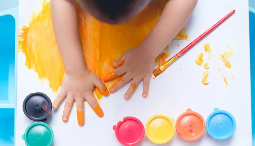 Manos pequeñas pintando con dedos y pincel. Un niño se divierte pintando con niños, rodeado de botes de pintura de colores.