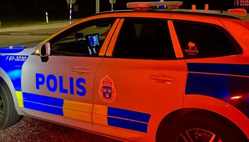 En polisbil med blåljus syns i mörkret. Texten "POLIS" är tydlig på sidan.