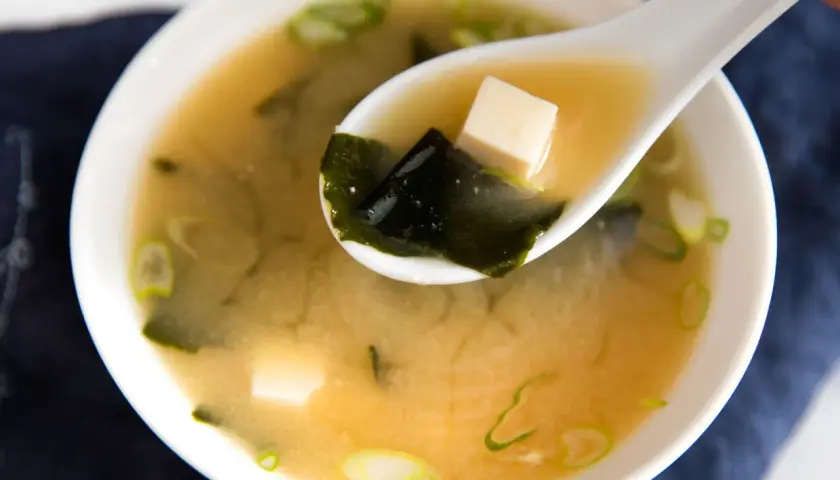 A spoonful of savory miso sauce soup, with tofu cubes and seaweed, ready to be enjoyed.