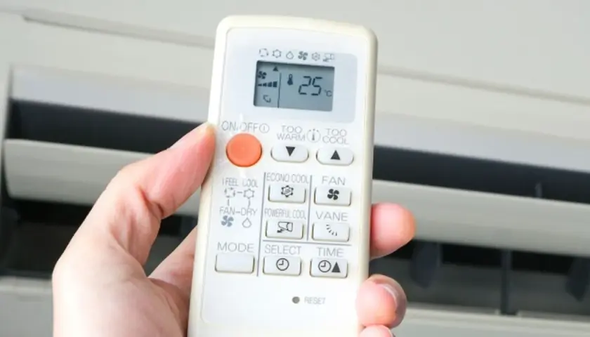 Mano sujetando control remoto de aire acondicionado. El símbolo del triángulo indica la función de enfriamiento.