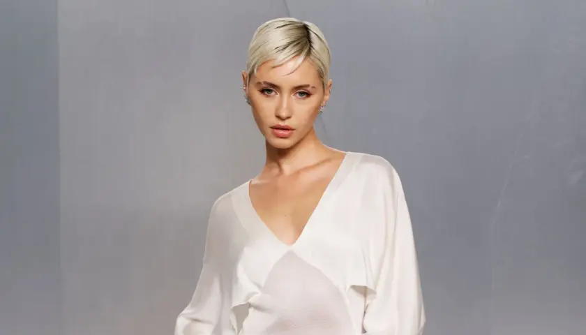 Iris Law, con su corte de pelo rubio platino y un top blanco de seda, posa con una mirada intensa.