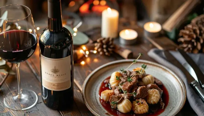 Un verre de vin rouge et une assiette de vin avec ris de veau, décorés de bougies et d'une cheminée en arrière-plan.
