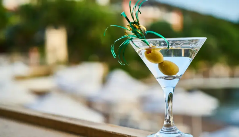 Idealny martini aperitivo z dwiema oliwkami, ozdobiony zielonymi wstążkami, na tle letniego krajobrazu.