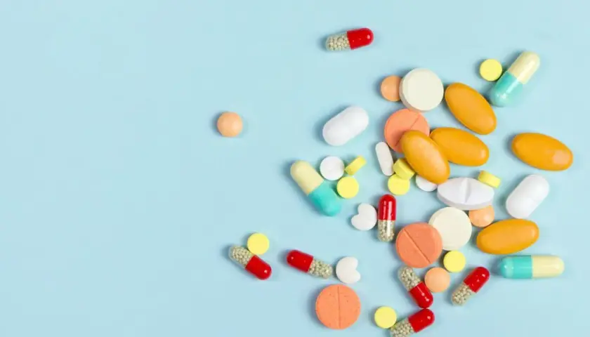 Różnorodne tabletki i kapsułki, w tym te przypominające milgamę, rozsypane na jasnoniebieskim tle.