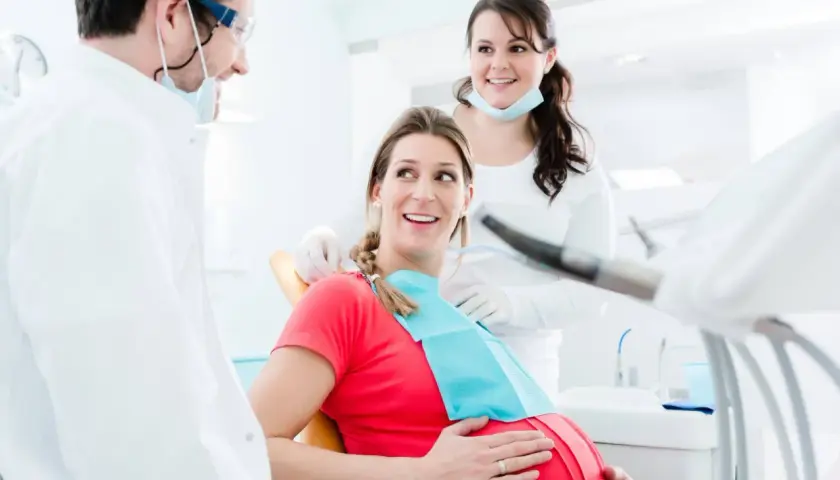 Uśmiechnięta ciężarna pacjentka u dentysty. Dba o zdrowie jamy ustnej, by uniknąć zapalenia dziąseł w ciąży.