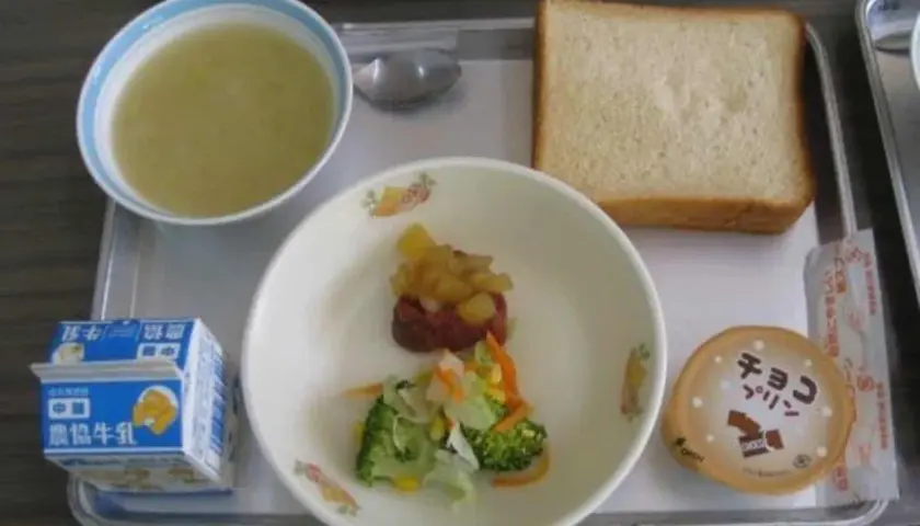 A typical Japanese school lunch tray with soup, bread, vegetables, meat, pudding, and milk.