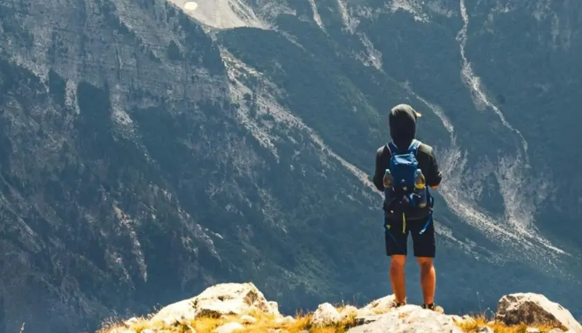 Ein Wanderer mit Rucksack steht auf einem Felsen und blickt in die majestätische Berglandschaft Albaniens.