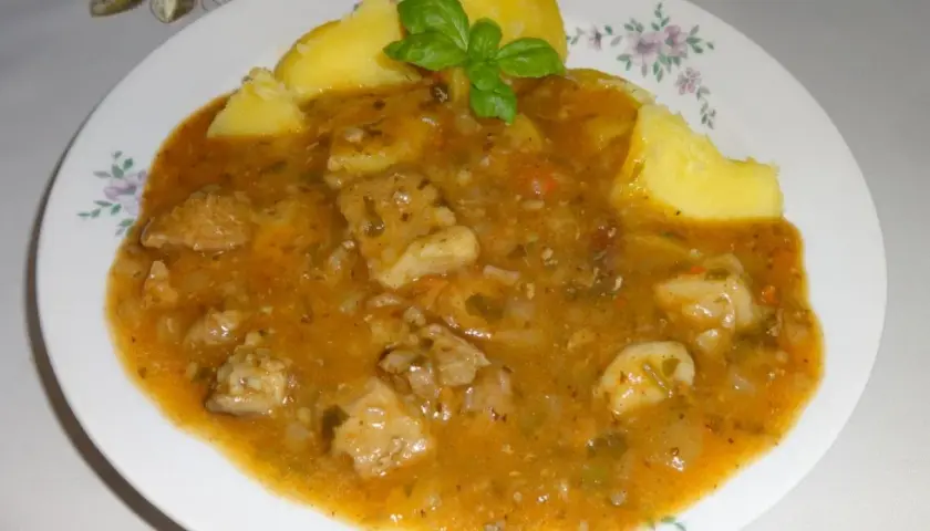 Pyszny sos do ziemniaków z kawałkami mięsa i warzyw, udekorowany listkiem bazylii.