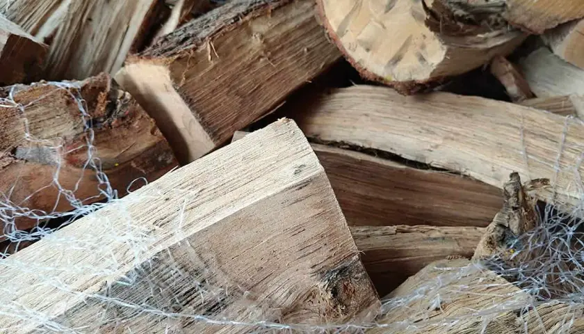 Un tas de bois sec, prêt à crépiter dans la cheminée. Les bûches sont emballées dans un filet blanc.
