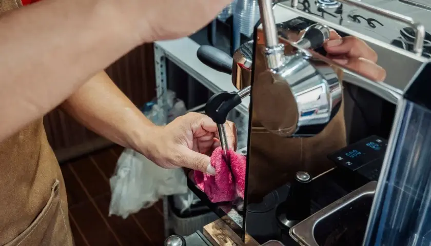 Ręce barista czyszczą dyszę ekspresu, przygotowując go do odkamieniania. Dbałość o sprzęt zapewnia idealne lattego.