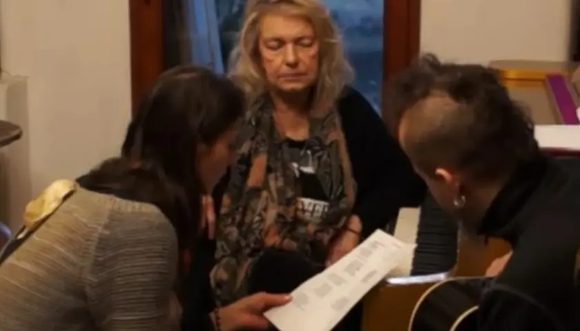 Katarzyna Gaertner z synem i młodą kobietą analizują nuty przy pianinie.