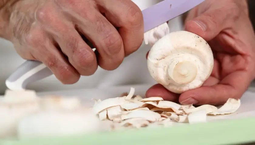 Dłonie obierają pieczarkę, tworząc stos cienkich skórek. Czy pieczarki się obiera? Tak, jeśli chcesz uzyskać delikatniejszy smak.