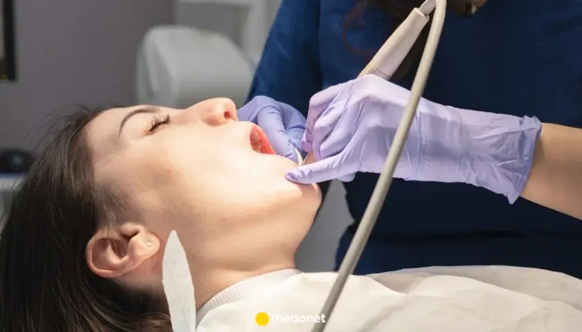 Dentysta w fioletowych rękawiczkach bada ząb pacjentki otwartymi ustami.