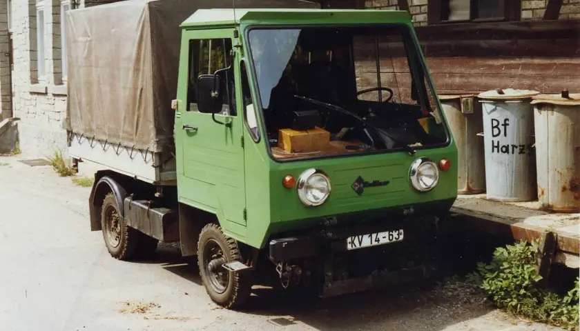 Zielony Multicar M25 z plandeką, gotowy do drogi. Obok śmietniki z napisem "Bf Harz".
