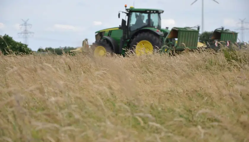 Grüner Traktor mit Anhängern im Feld, bereit für die Ernte. Die Kfz-Steuer für diesen Traktor ist ein wichtiger Faktor für Landwirte.