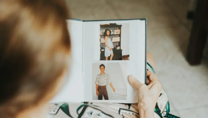 Osoba przegląda fotoksiążkę z dawnymi zdjęciami. Widać ciążowy brzuch i młodego mężczyznę. To inspiracja, jak zrobić fotoksiążkę.