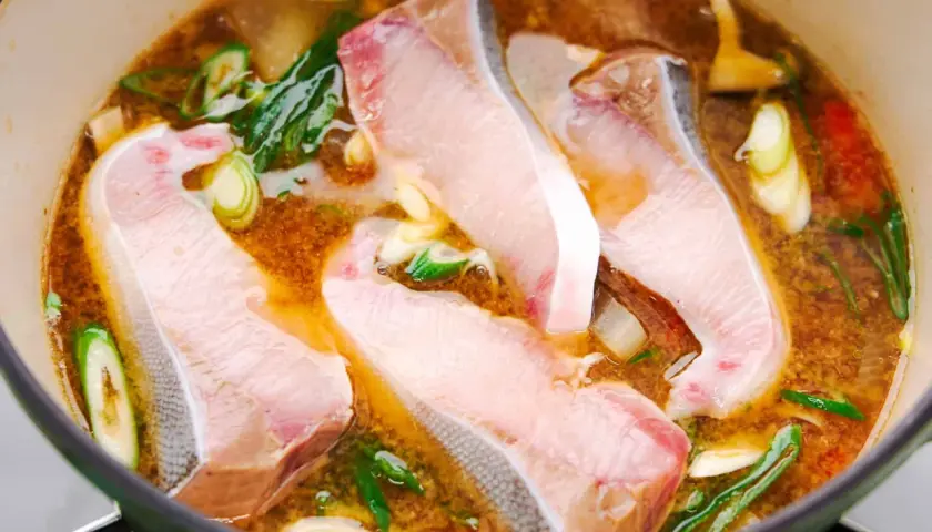 A pot of simmering Japanese fish soup with tender white fish fillets, green onions, and ginger.