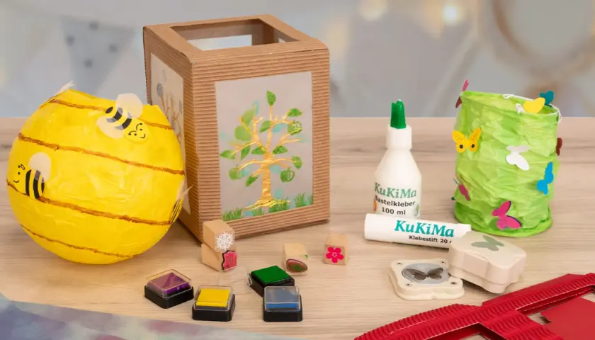 Bastelmaterialien für eine St. Martin Laterne: Bienen-Laterne, Baum-Laterne, Kleber, Stempel und Schmetterlingsstanzer.