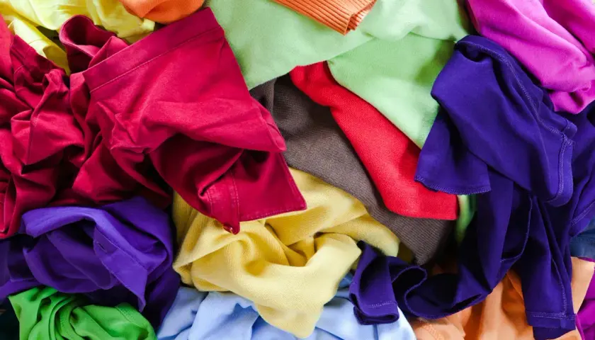 Bunte Stoffe, bereit für T-Shirt Upcycling. Ein Berg aus Rot, Lila, Grün, Gelb und Orange lädt zum kreativen Gestalten ein.