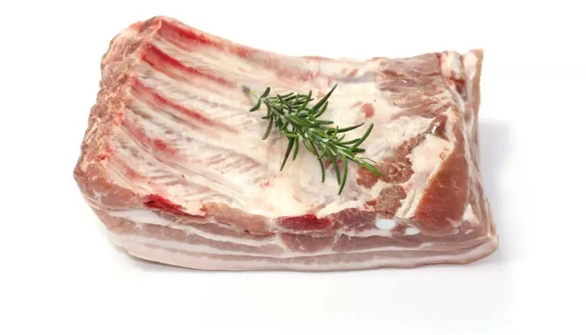Un morceau de poitrine de porc frais, avec des côtes apparentes et une branche de romarin posée dessus, prêt à être cuisiné.