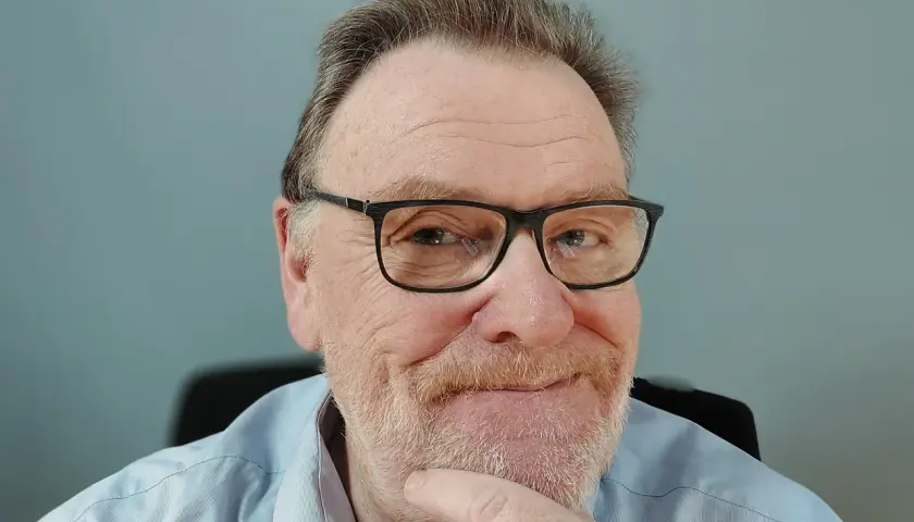 Porträt eines älteren Mannes mit Brille und Bart, der nachdenklich seinen Finger am Kinn hat.