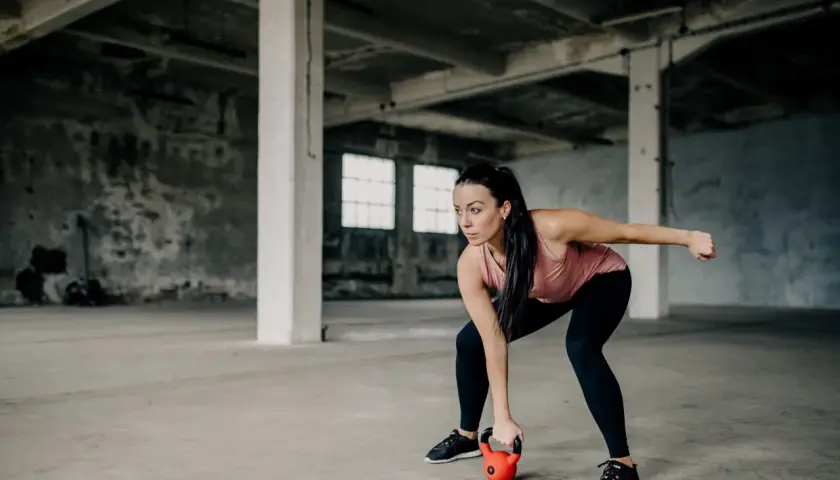 Kobieta w koszulce treningowej wykonuje ćwiczenie z kettlebell w opuszczonej hali.