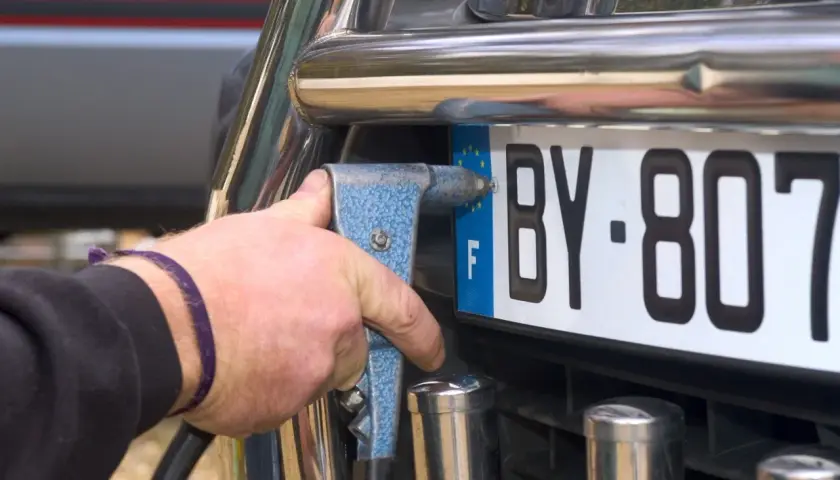 Mano con rivettatrice che fissa una targa auto, forse per cambiare targa auto per sfizio.