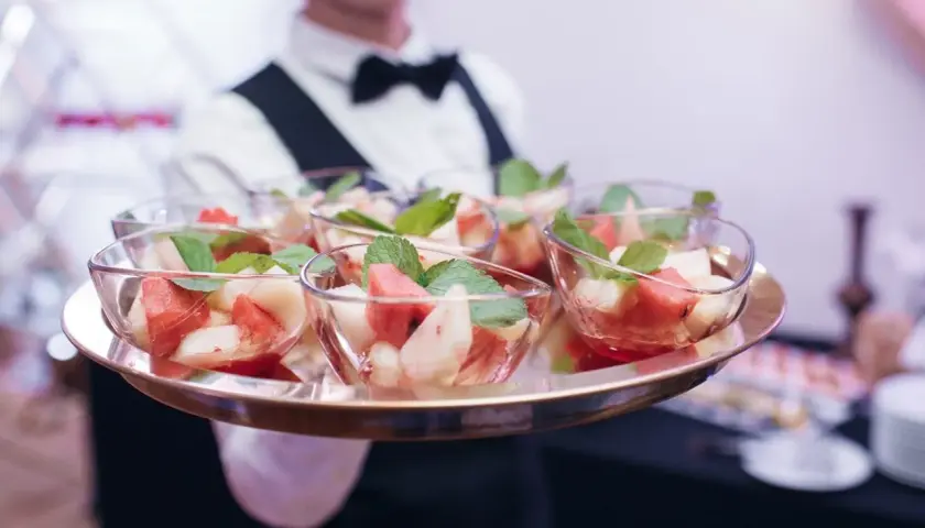 Kelner niesie tacę z owocowymi deserami. Zastanawiasz się, ile kosztuje catering firmowy?