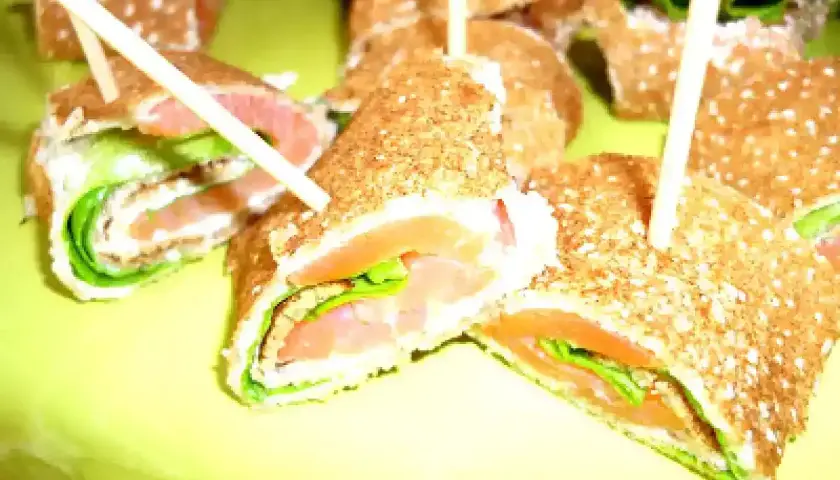 Rouleaux de galette sarrasin garnis de saumon fumé et de salade verte, servis sur une assiette jaune vif.