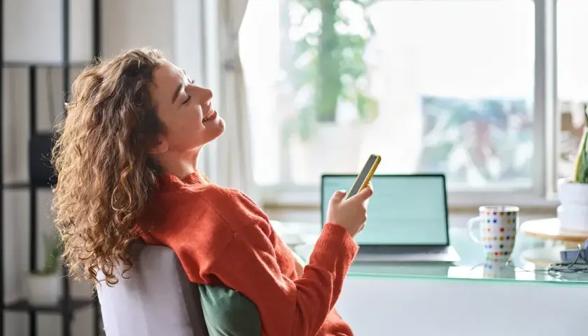 Kobieta z kręconymi włosami śmieje się, trzymając telefon. Czy 3 maja można pracować? Ona chyba odpoczywa.
