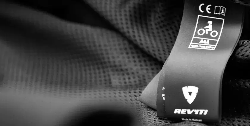Etichetta con simboli di sicurezza e certificazione casco moto AAA, marchio REV'IT!.