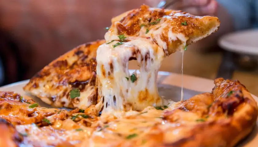 Ein Stück Pizza mit geschmolzenem Käse wird hochgehoben. Die vielen Pizza Kalorien sind es wert!