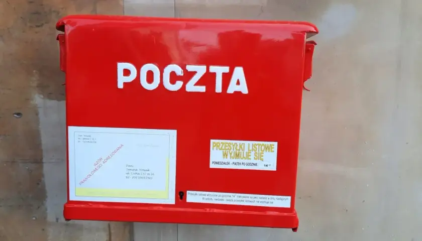 Czerwona skrzynka pocztowa z napisem "POCZTA". Obok etykieta z adresem i informacją, czy żona może odebrać list polecony z sądu.