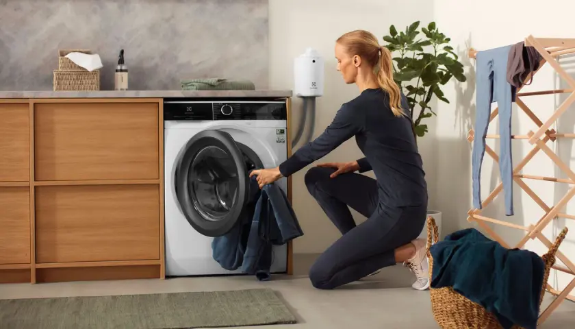 Femme chargeant du linge dans une machine, dont un vêtement en matière PBT, dans une buanderie moderne.