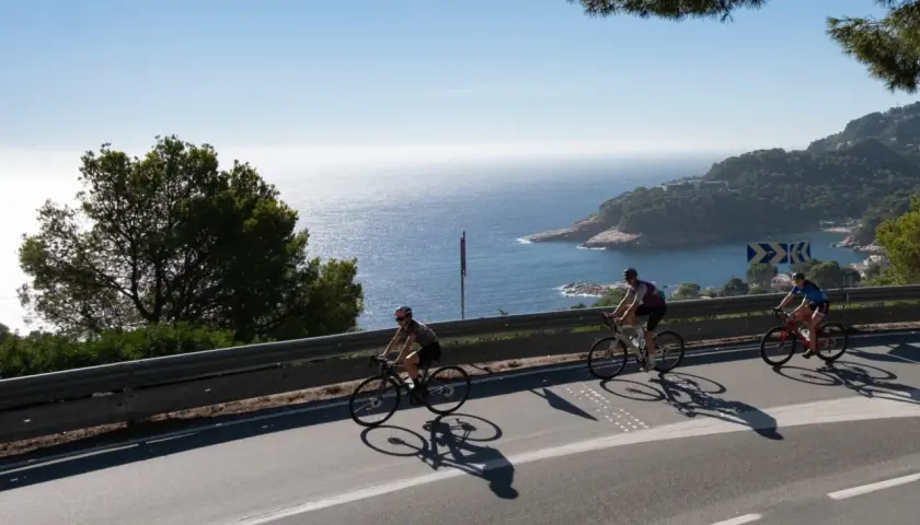 Ciclistas disfrutan del cicloturismo en Girona, con vistas al mar Mediterráneo y la costa.