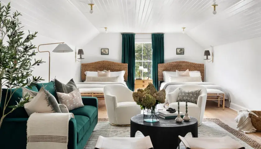 Two beds flank a window with teal curtains. Multiple rugs define the seating and sleeping areas in this cozy room.