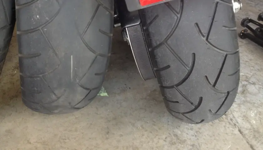 Dos ruedas de moto, una rueda moto gastada con dibujo casi liso y otra con más surcos, sobre suelo de hormigón.