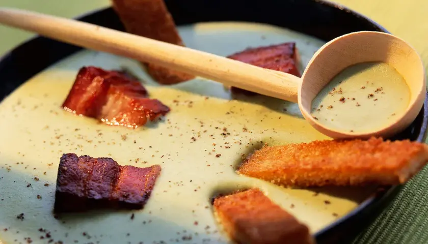 Une cuillère en bois sert une soupe de pois cassés onctueuse, garnie de lard croustillant et de croûtons dorés.